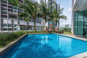 A modern building with a swimming pool, palm trees, and a colorful play structure. - I City Premier Suites Shah Alam (Shah Alam)