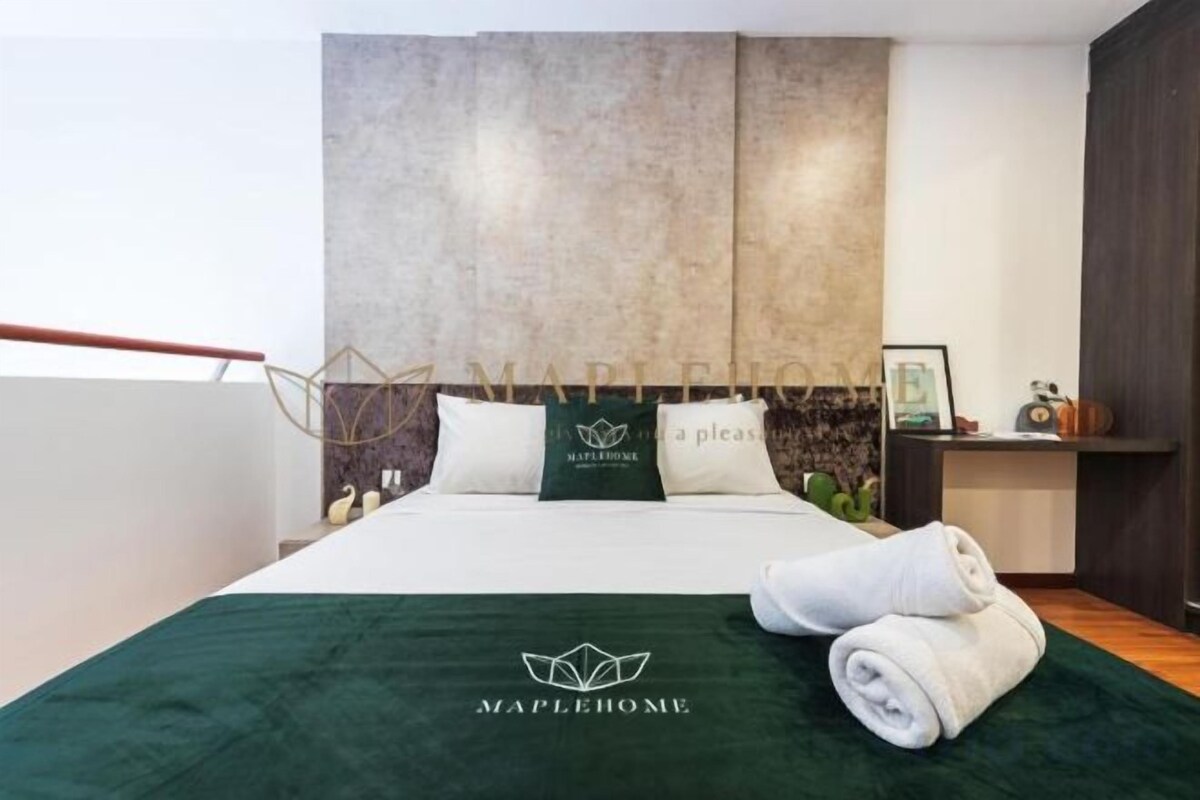 A hotel room with a bed, a green bedspread, two pillows, a headboard, a nightstand, and a framed picture.