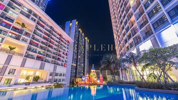 A modern hotel with a large pool, multiple balconies, and a decorative structure in the pool area.