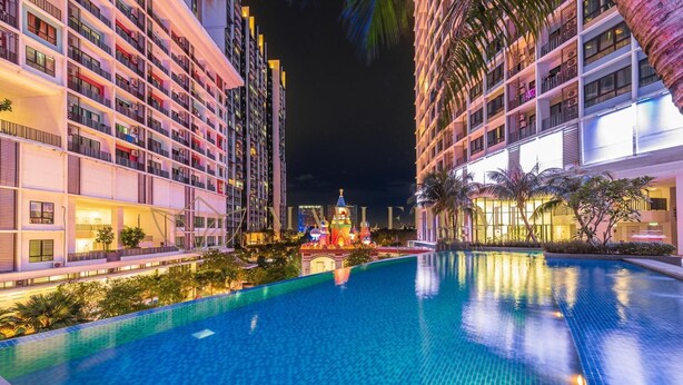 Vista nocturna de un hotel con piscina, varios balcones y un edificio decorativo al fondo.