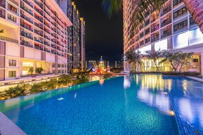 Une vue nocturne d’un hôtel doté d’une piscine, de nombreux balcons et d’un bâtiment décoratif en arrière-plan.
