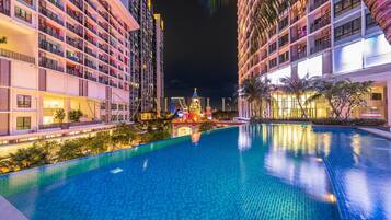 A nighttime view of a hotel with a swimming pool, multiple balconies, and a decorative building in the background.