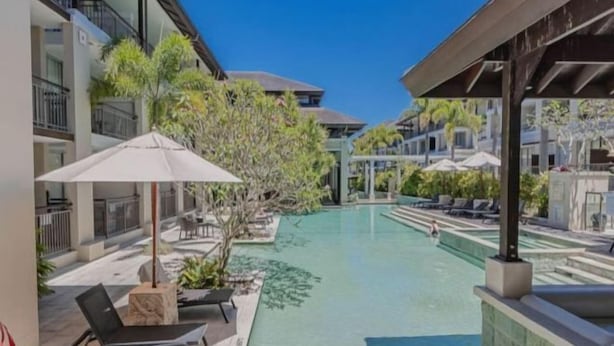 A pool area with lounge chairs and umbrellas, surrounded by buildings with balconies. - Santai Resort - Holiday Management (Casuarina)