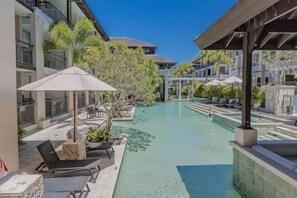 Ein Poolbereich mit Liegestühlen und Sonnenschirmen, umgeben von Gebäuden mit Balkonen.
