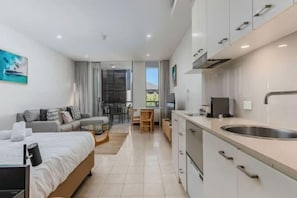 Ein modernes Hotelzimmer mit Bett, einer kleinen Sitzecke, einer Küchenzeile und Blick ins Freie.