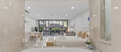 A modern bathroom with a large bathtub, a seating area with a sofa, and a dining area in the background.