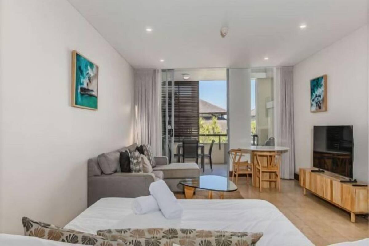 A modern hotel room with a bed, sofa, dining table, chairs, TV, and artwork.