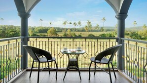 A balcony with two wicker chairs and a small table, overlooking a lush landscape with palm trees and open fields. - Sahaswara Luxury Resort (Anjuna)