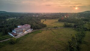 An aerial view of a building with a large open area in front, surrounded by greenery and hills in the distance. - Sahaswara Luxury Resort (Anjuna)