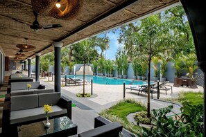 Área da piscina com assentos, piscina e vegetação ao redor.