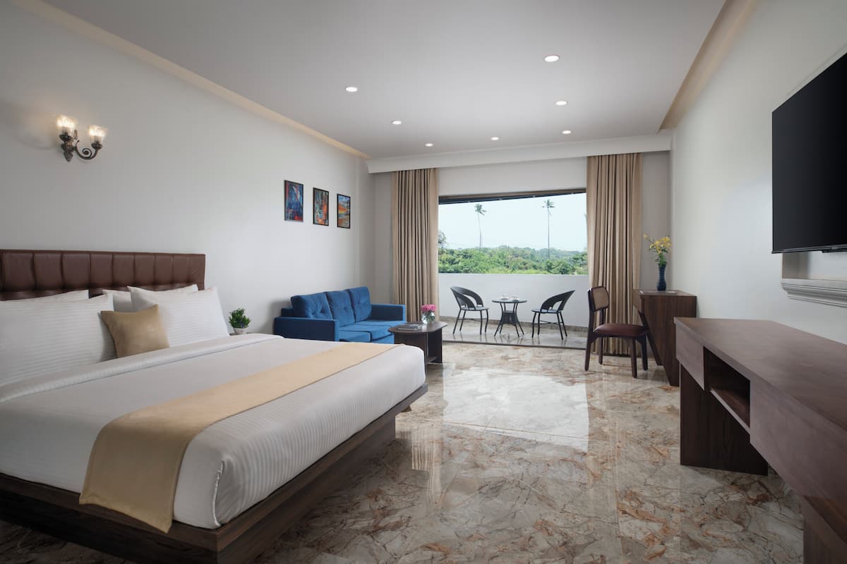 A hotel room with a large bed, a sofa, a desk, a TV, and a balcony with a view.