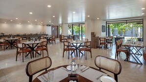 A spacious dining area with multiple tables and chairs, large windows, and a modern interior design. - Sahaswara Luxury Resort (Anjuna)