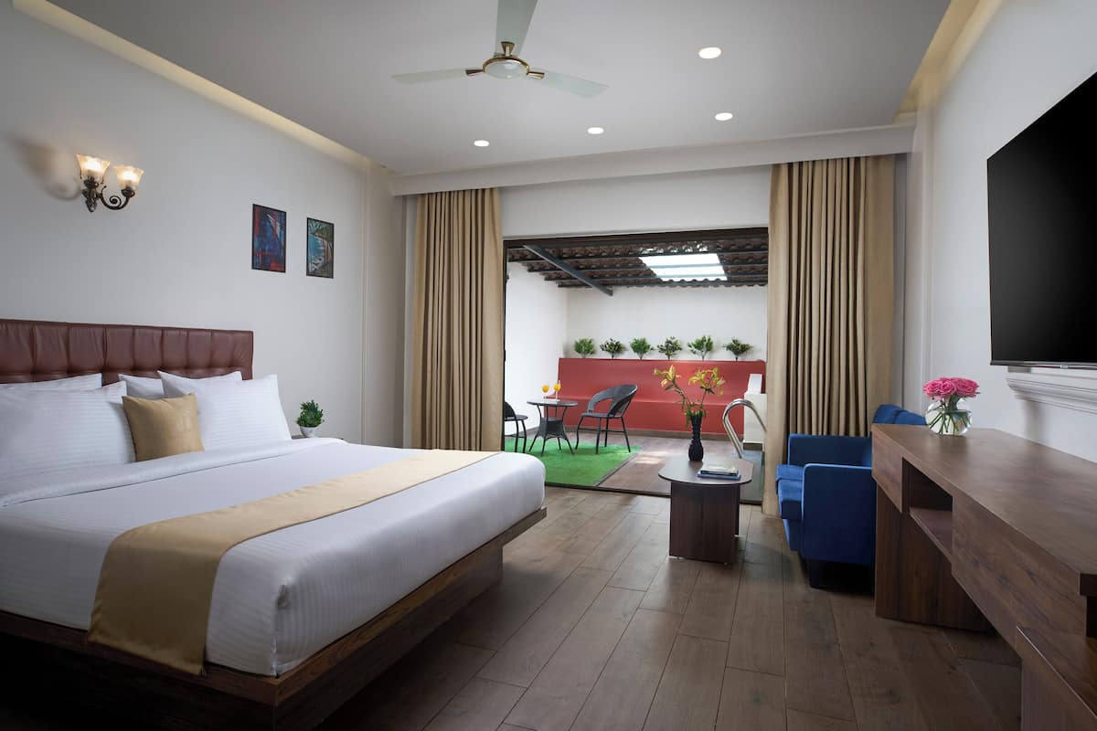 A hotel room with a large bed, a desk, a chair, a TV, and a balcony with a view.