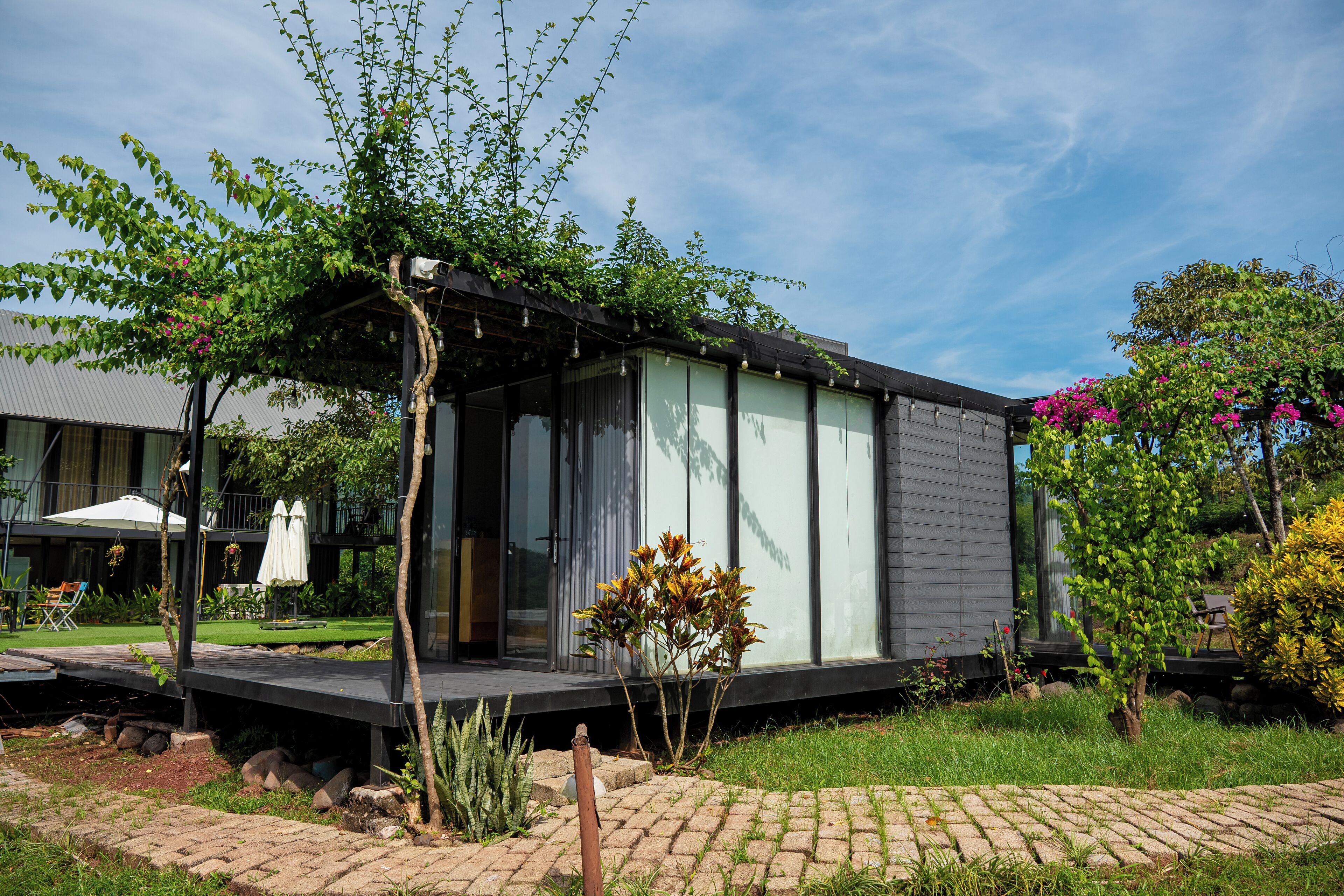 A modern house with a covered porch, a garden with various plants, and a clear blue sky.