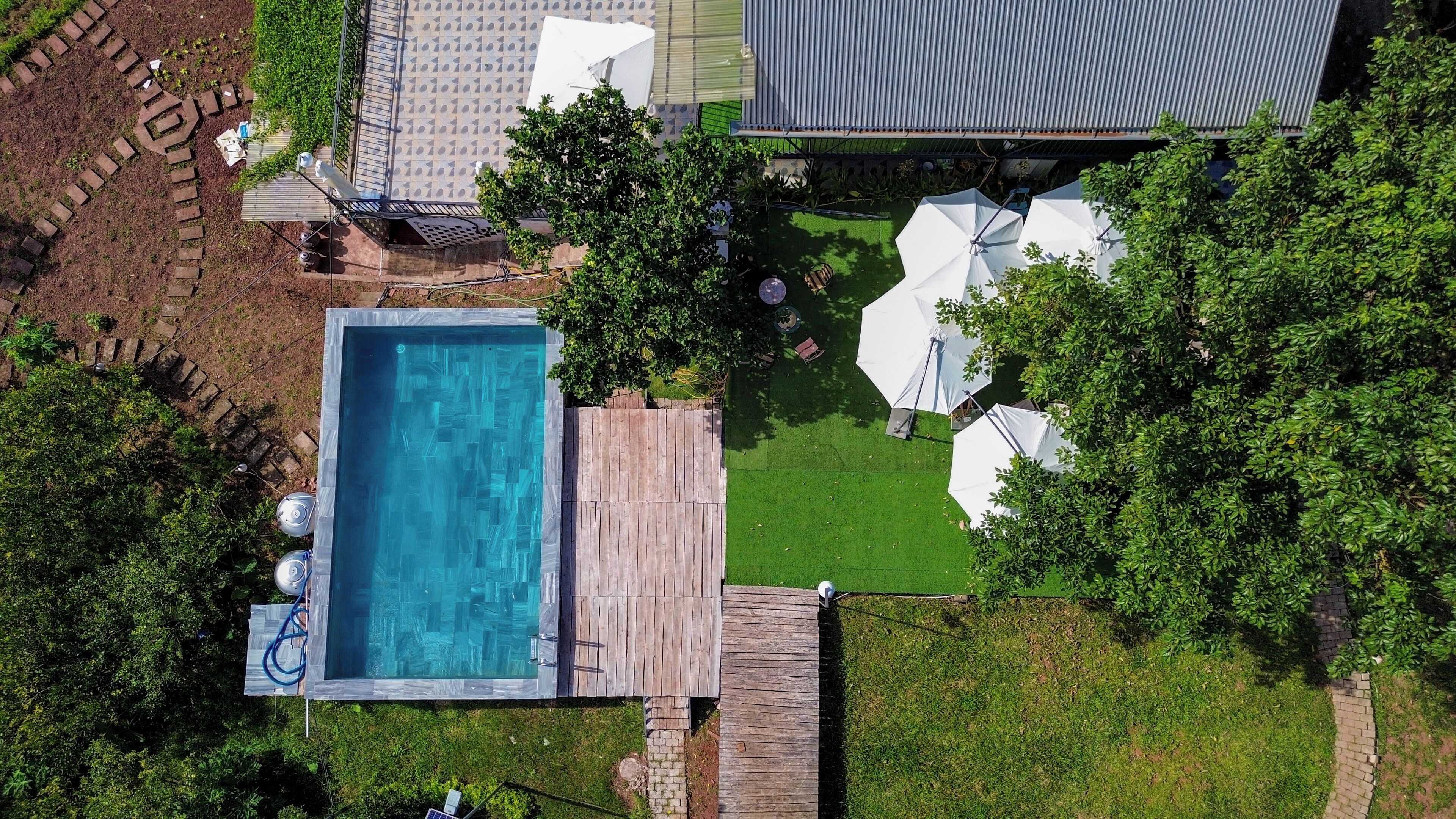 An aerial view of a backyard with a swimming pool, a wooden deck, and a grassy lawn.
