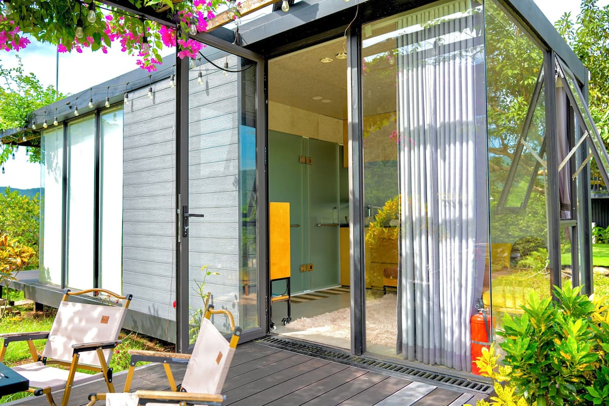 Una casa moderna con un amplio ventanal corredera que da a un patio con mobiliario exterior.