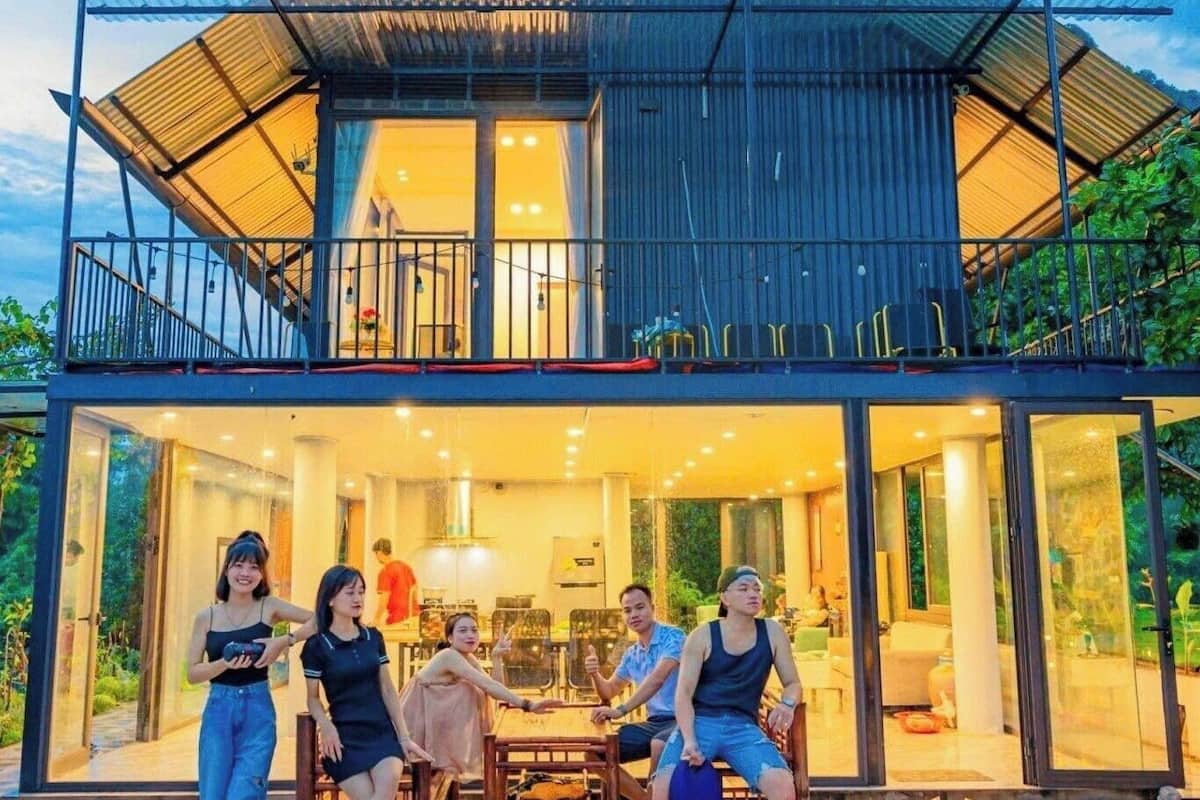 Una casa moderna con fachada de vidrio, un área de comedor con mesa y sillas, y un balcón con barandilla.