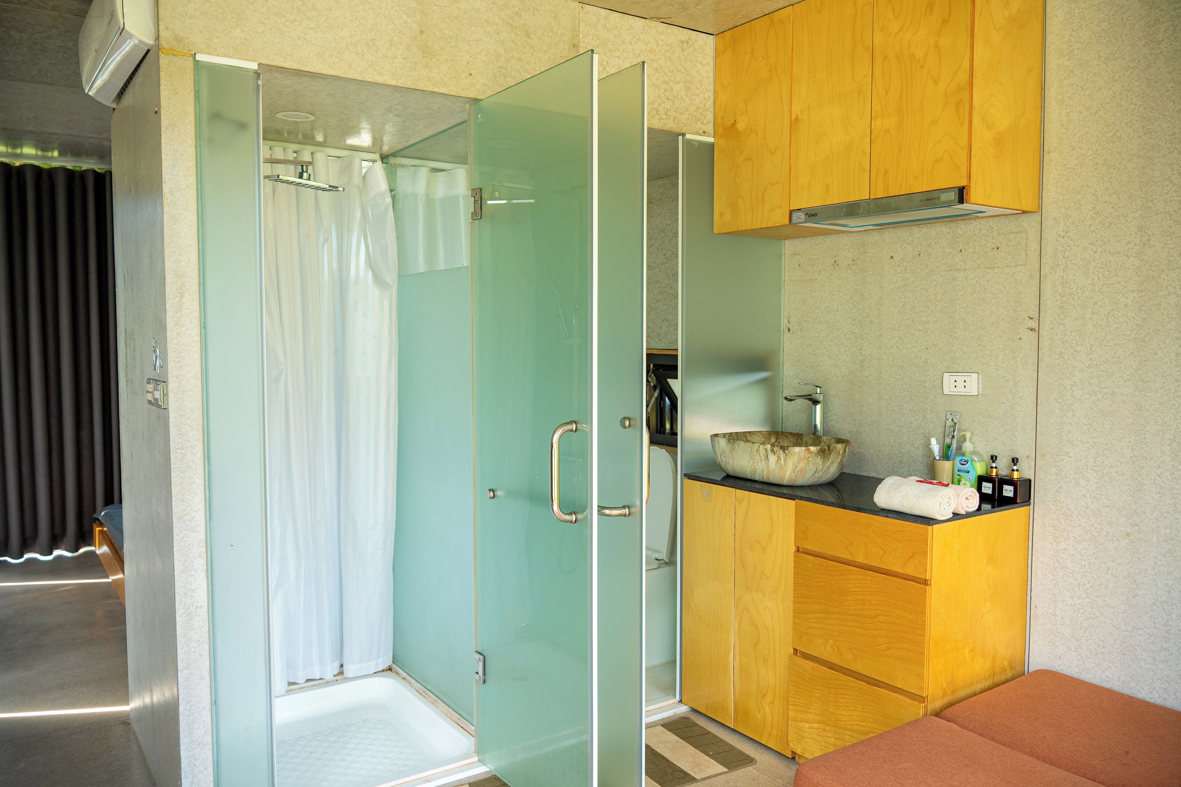 A bathroom with a glass shower enclosure, wooden cabinets, and a sink with toiletries.