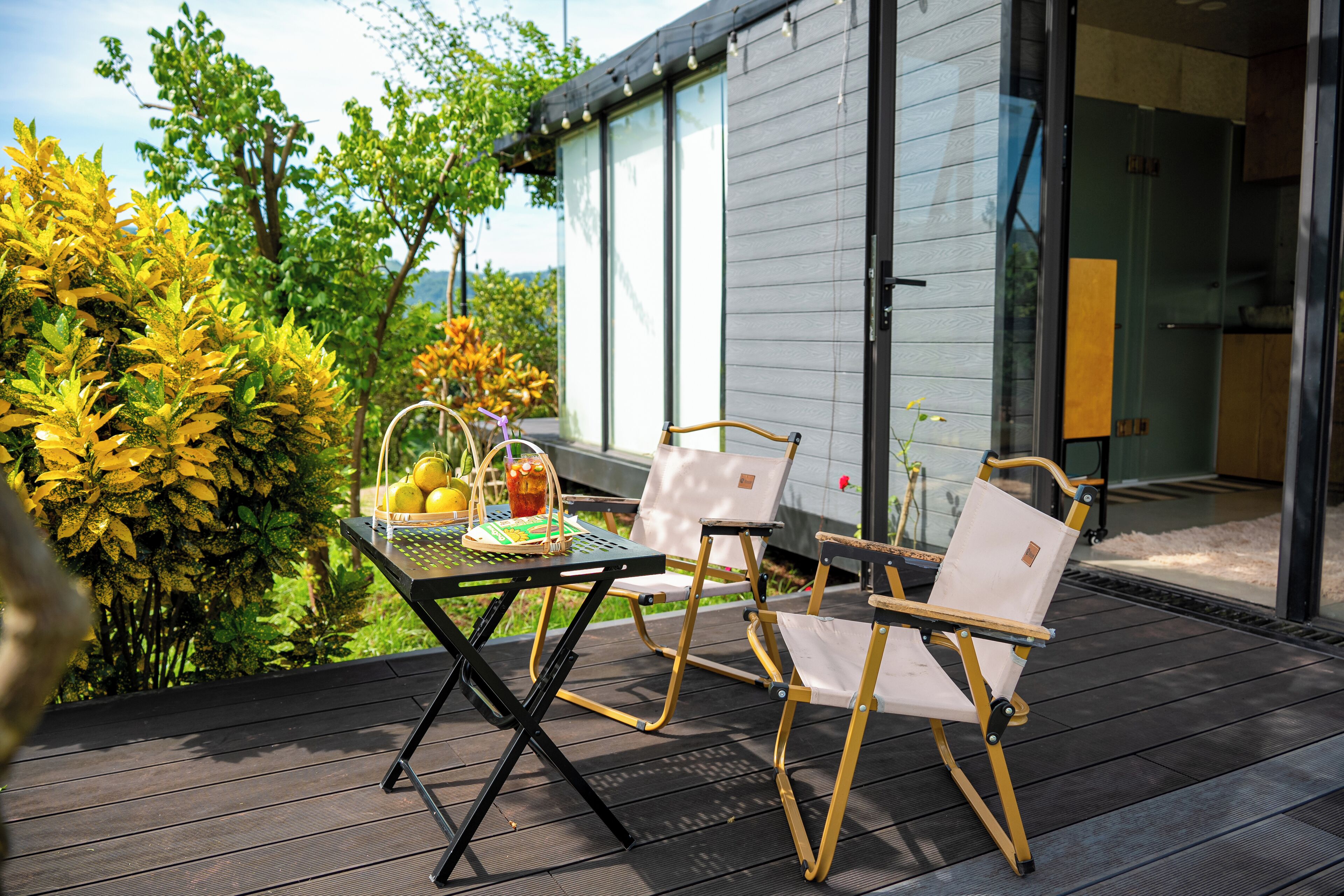 An outdoor patio with a table and two chairs, a basket of fruit, and a glass of drink.