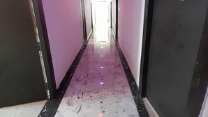 A hallway with a reflective floor, doors on both sides, and ceiling lights. - Happy Palace Resort (Gaya)