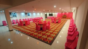 A spacious hall with a patterned floor, rows of pink-covered chairs, and tables set for events. - Happy Palace Resort (Gaya)