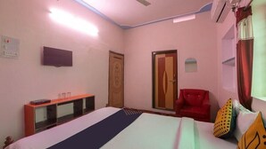 A hotel room with a bed, a red armchair, a TV, and a window with curtains. - Happy Palace Resort (Gaya)