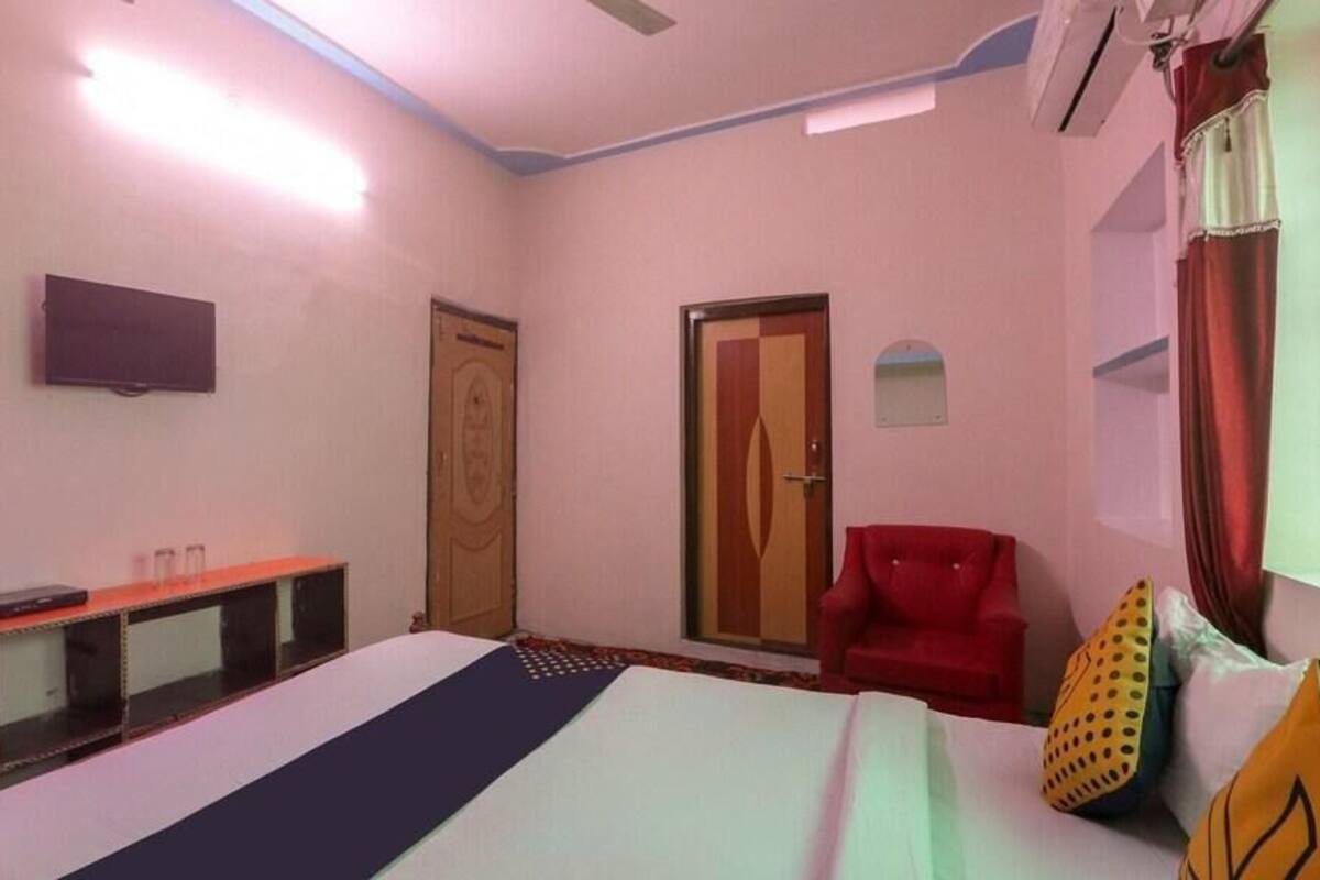 Une chambre d’hôtel avec un lit, un fauteuil rouge, une télévision et une fenêtre avec des rideaux.