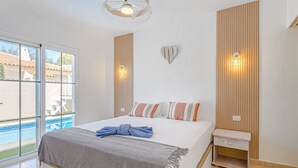 A bedroom with a bed, a nightstand, a wall-mounted light, and a view of a swimming pool. - Mila Moon by Interhome (Callao Salvaje)