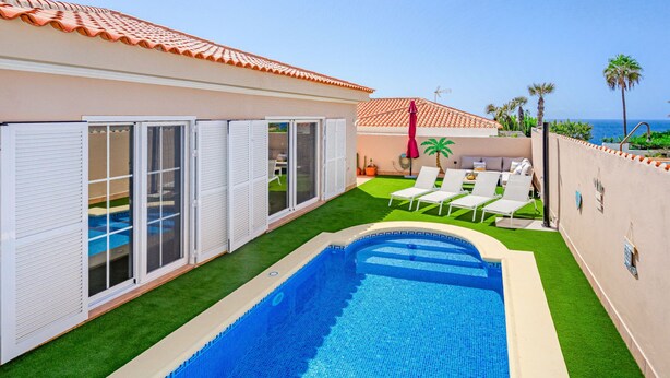 A swimming pool with a tiled deck, a covered patio with chairs, and a view of the sea. - Mila Moon by Interhome (Callao Salvaje)