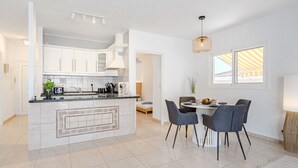 A modern kitchen with white cabinets, a central island, and a dining area with two chairs and a table. - Mila Moon by Interhome (Callao Salvaje)