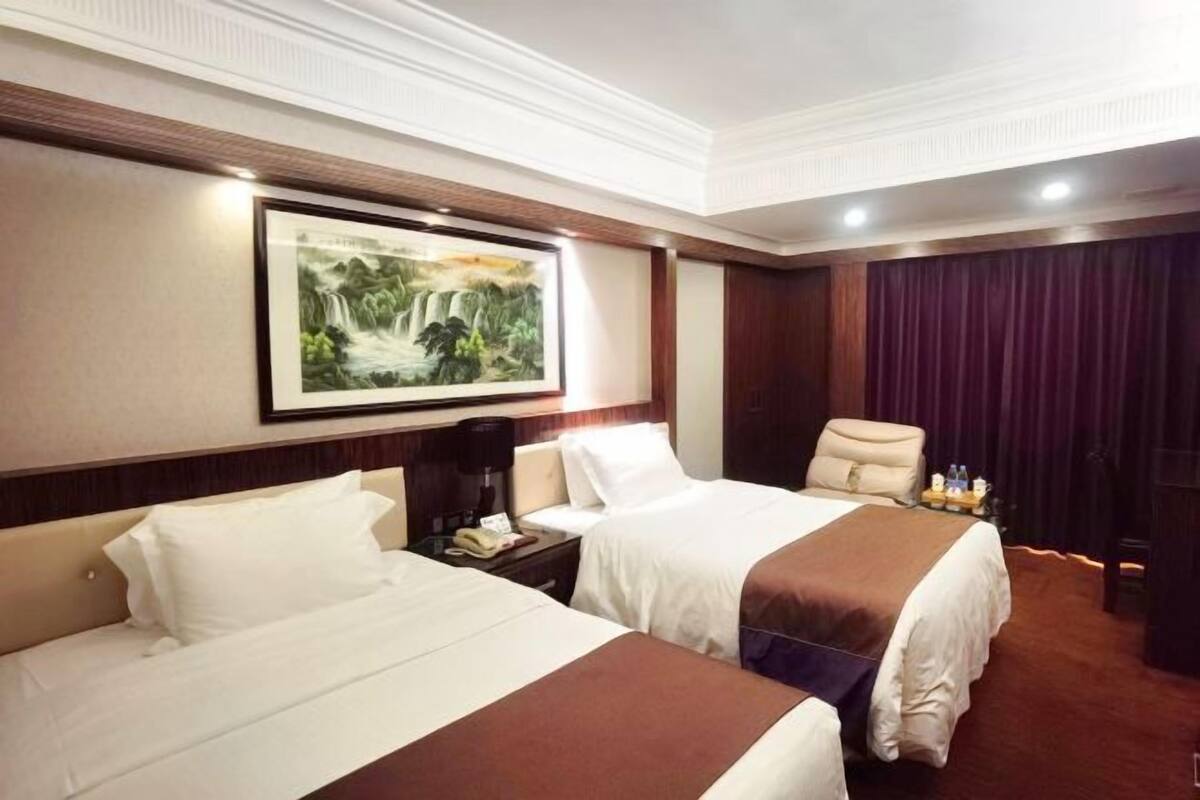 A hotel room with two beds, a large painting on the wall, a desk with a phone, and a chair.