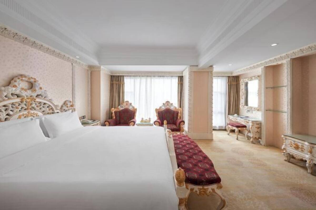 A hotel room with a large bed, two armchairs, a vanity with a mirror, and a small table.