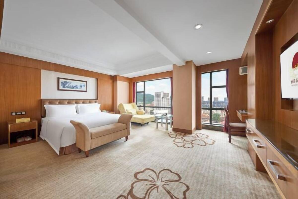 A hotel room with a large bed, a TV, a balcony with a view, and a wooden wall.