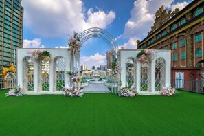 Un arco nupcial adornado con flores y una fuente, con un edificio de ventanas arqueadas al fondo.