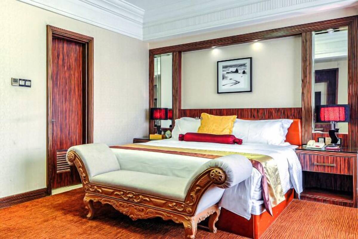 A hotel room with a large bed, a wooden bench, a nightstand, and a framed picture on the wall.