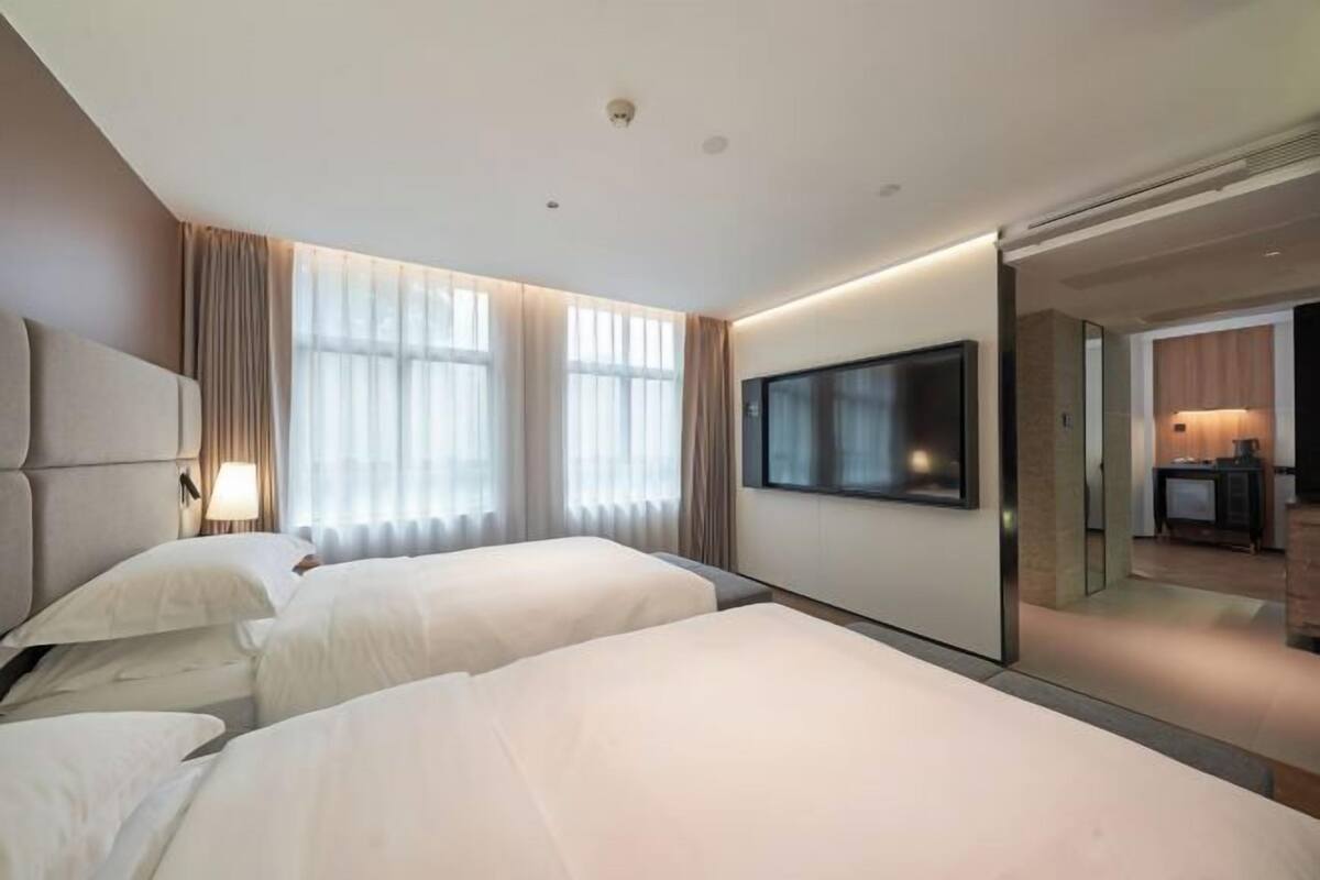 A hotel room with two beds, a large flat-screen TV, and a sliding door leading to a bathroom.
