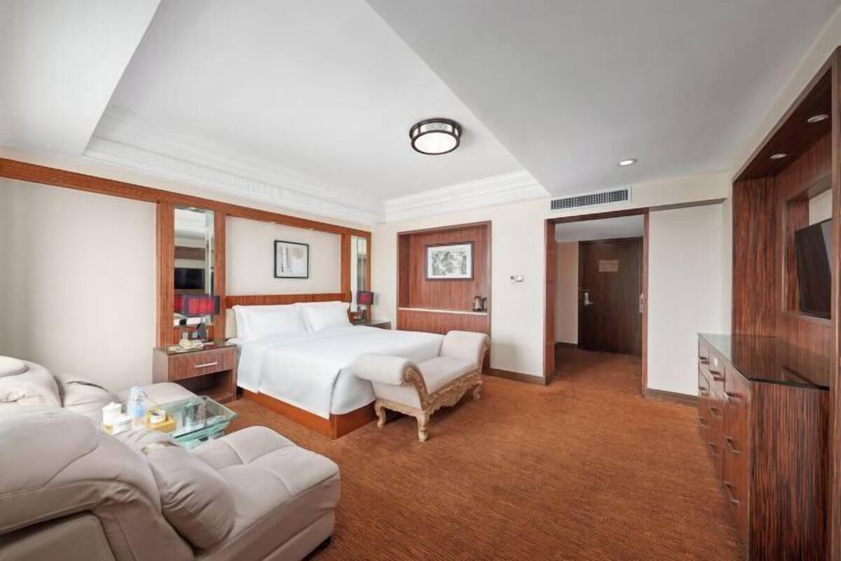 A hotel room with a large bed, a sitting area with a sofa, a small table, and a TV.