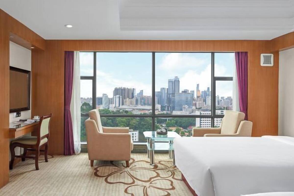 Une chambre d’hôtel avec vue sur les toits de la ville, un lit, deux chaises, un bureau et une petite table.