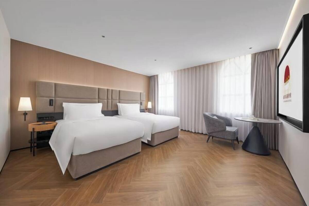 A hotel room with two beds, a desk, a chair, and a small table.