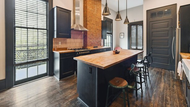A modern kitchen with a large island, black cabinetry, a brick accent wall, and a large window with blinds. - Chic 2-bedroom apartment in eclectic Bywater with AC, WiFi (New Orleans)