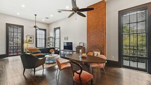 A spacious living room with a dining area, large windows, and a brick accent wall. - Chic 2-bedroom apartment in eclectic Bywater with AC, WiFi (New Orleans)