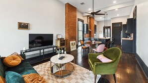 A spacious living area with a large TV, a dining table, and a kitchen in the background. - Chic 2-bedroom apartment in eclectic Bywater with AC, WiFi (New Orleans)