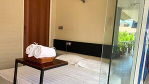 Habitación de hotel con cama, una mesita con toallas, cabecera de madera y puerta de cristal que da a un espacio exterior.