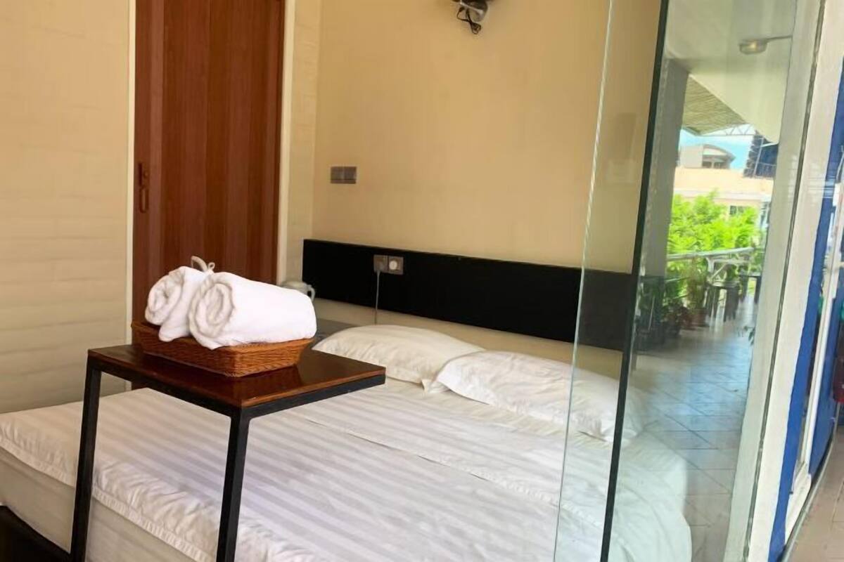 Habitación de hotel con cama, una mesita con toallas, cabecera de madera y puerta de cristal que da a un espacio exterior.
