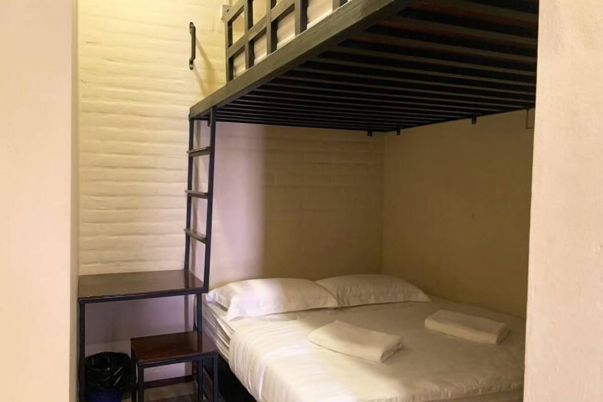 Una cama litera con escalera, una mesita pequeña y un cubo de basura.