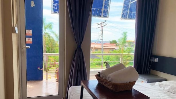 Habitación de hotel con cama, una mesita con una cesta de toallas, ventana con cortinas y vistas a zonas verdes.