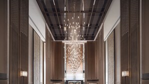 Un hall d’entrée moderne avec un sol à motifs géométriques, un lustre central et des espaces de détente de part et d’autre.