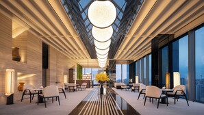 Un moderno vestíbulo de hotel con una larga recepción, asientos cómodos y grandes ventanales con vistas a la ciudad.
