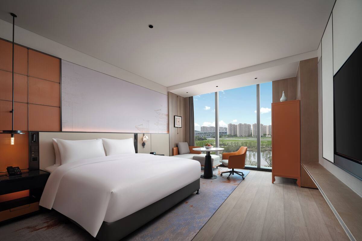 A modern hotel room with a large bed, a desk, a chair, and a TV.
