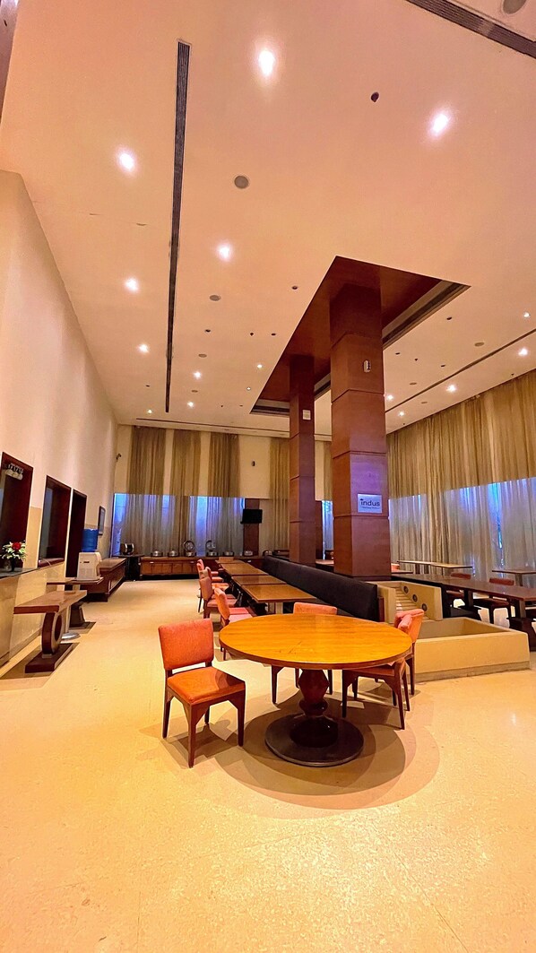 A spacious indoor area with multiple tables and chairs, a long counter, and a large pillar. - The Sky Imperial Jaipur (Amer)